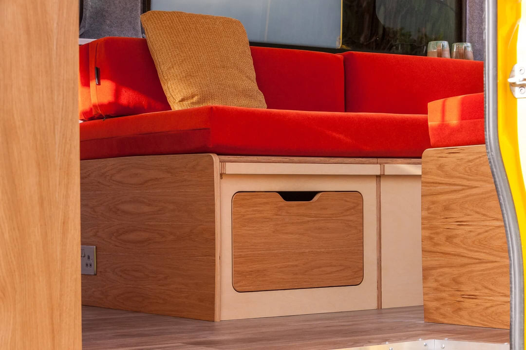 Campervan “Swale” Benches detailed view of extended storage drawer with camping gear beneath red bench seat inside campervan.