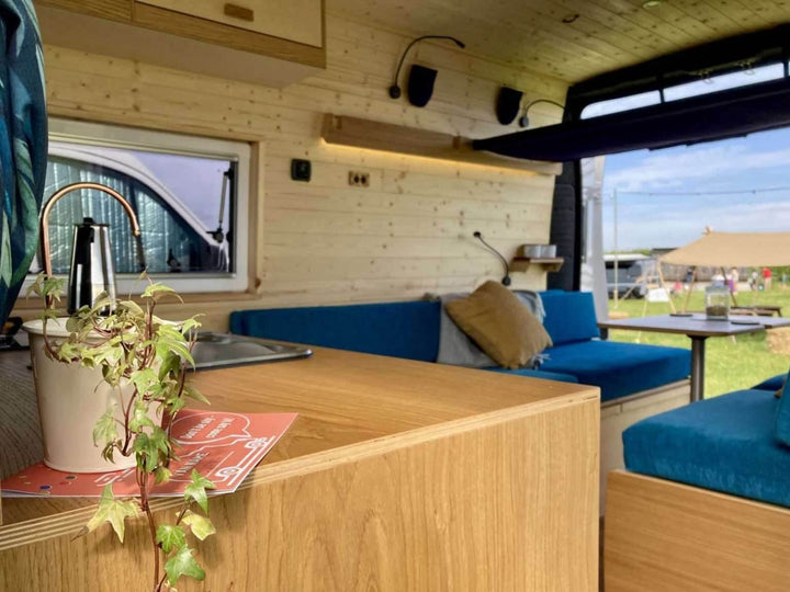 Campervan “Swale” Benches rear interior view with twin red benches and storage bases installed inside yellow campervan, rural stone house background.