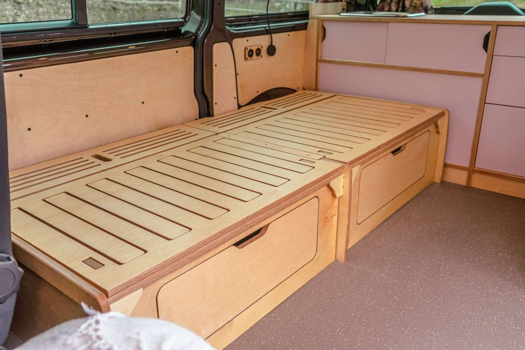Campervan “Topo” Sofa-Bed fully extended into a flat bed platform inside a campervan with light wood cabinetry.