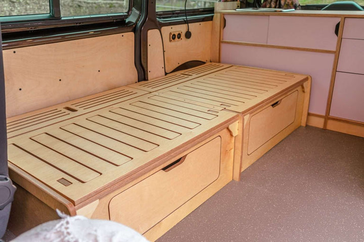 Campervan “Topo” Sofa-Bed fully extended into a flat bed platform inside a campervan with light wood cabinetry.