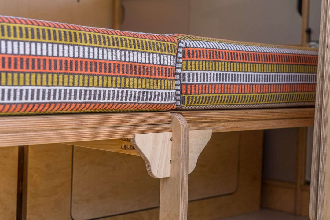 Campervan “Topo” Sofa-Bed furniture kit installed in a campervan with storage drawers and shelving, rear doors open to an outdoor landscape.