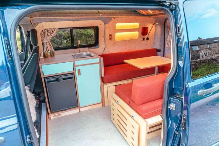 Rear view of the campervan interior featuring the Campervan Helm Kitchen Unit with fold-out table and bench seating.
