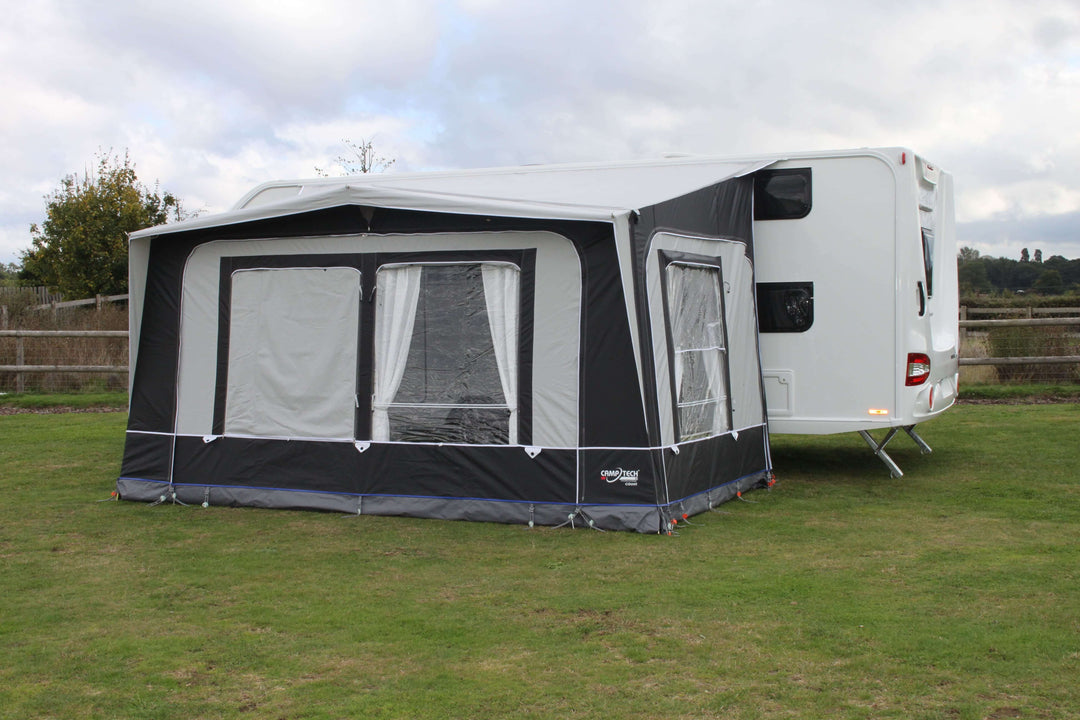 Camptech Count DL  porch awning with clear panels and side door, attached to a caravan on a green grassy field at a campsite.