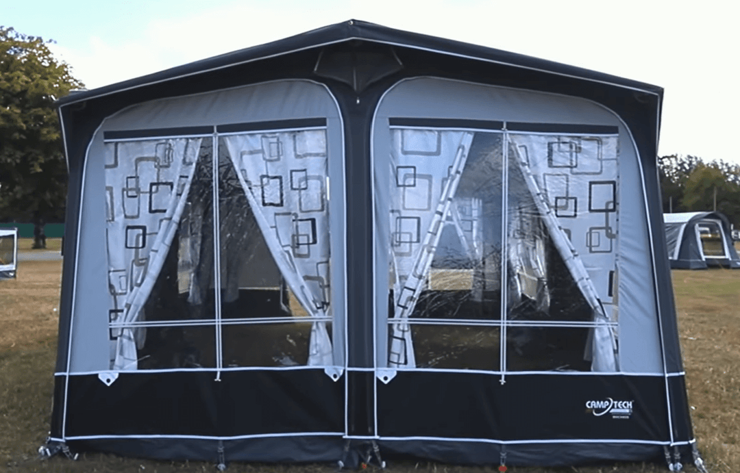 Camptech Duchess 340 porch awning with modern geometric curtains and clear front windows, displayed on a campsite under a blue sky.