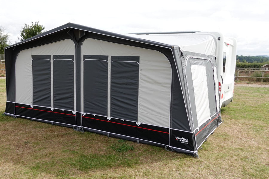 Camptech Mayfair DL Seasonal Caravan Awning with all windows fully covered, attached to a white caravan, set on a grassy pitch under a cloudy sky.
