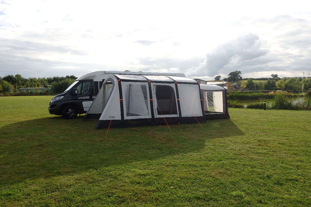 Camptech Moto Canterbury campervan awning with front canopy and multiple panels, shown on a grassy campsite beside a black and white motorhome.