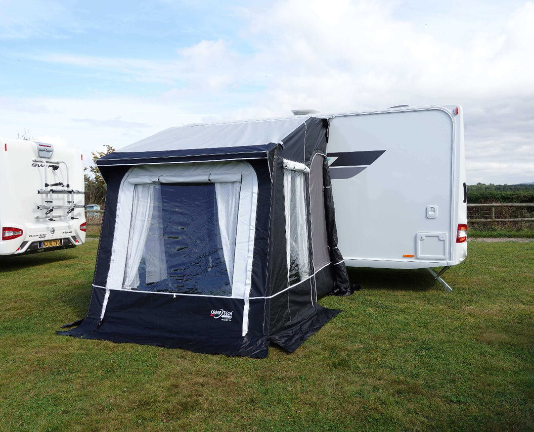 Camptech Princess DL porch awning attached to a caravan on a grassy campsite, featuring clear windows, white curtains, and modern black and grey design under a bright sky.