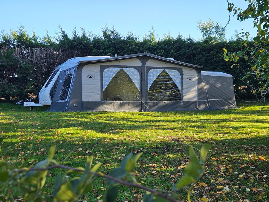 Side view of the Sunncamp Casa Full Touring Poled Awning fully installed on a caravan on grass with trees and greenery in the background.