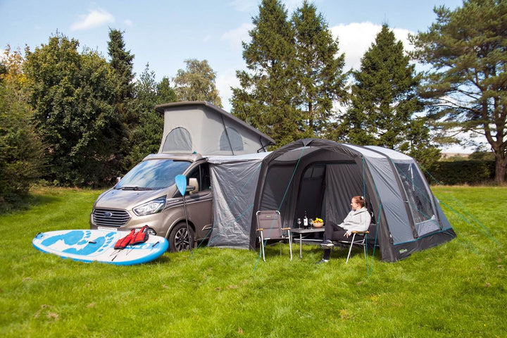 Angled front view of the Outdoor Revolution Cayman Air T3 Lite driveaway awning set up beside a campervan with camping chairs and table.