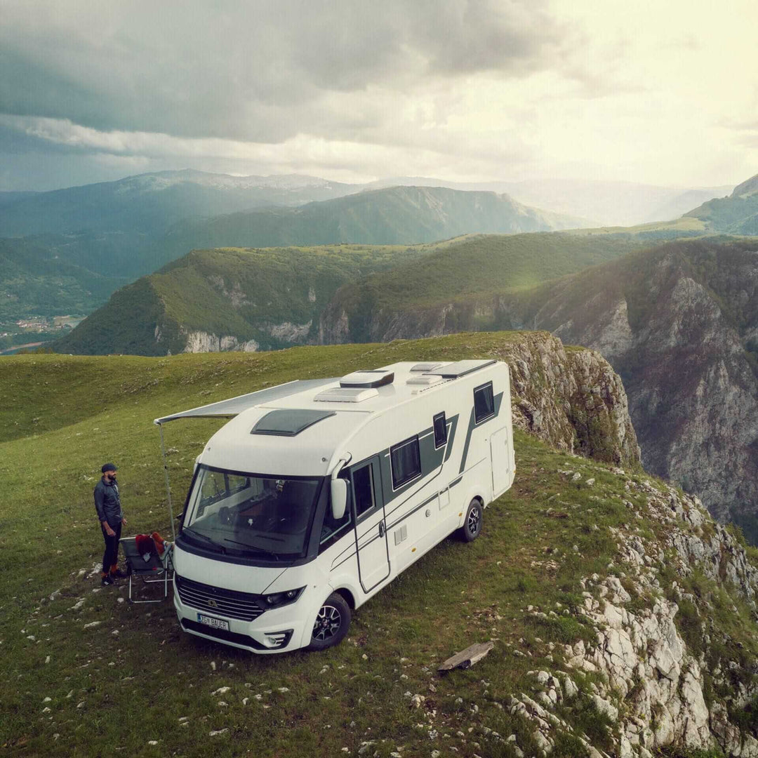 Dometic FreshJet FJX4 1500M Air Conditioner mounted on a motorhome rooftop parked on a grassy cliff with mountain landscape and cloudy sky in the background.