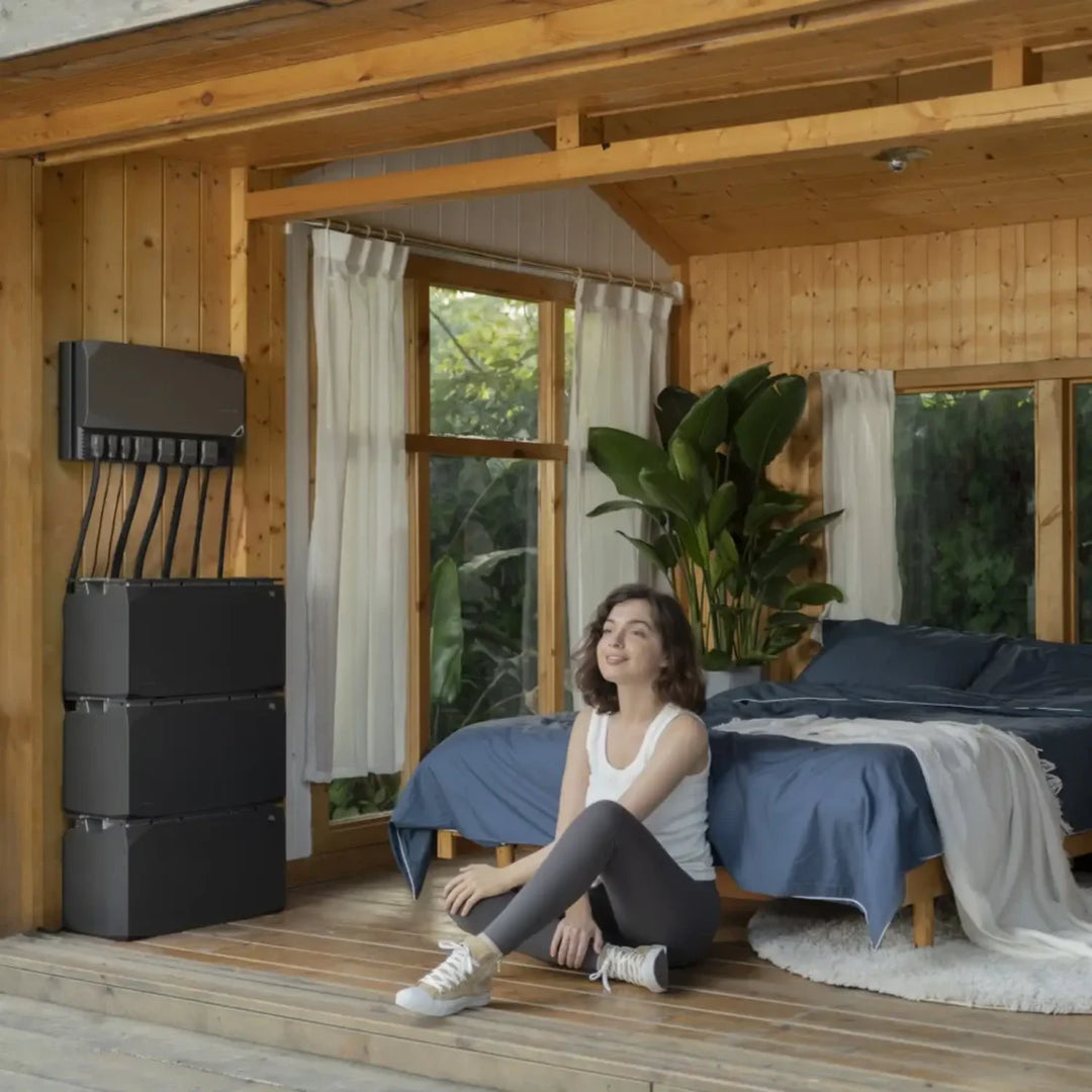 EcoFlow Independence Kit installed inside a modern wooden cabin bedroom with woman relaxing beside the stacked power system.