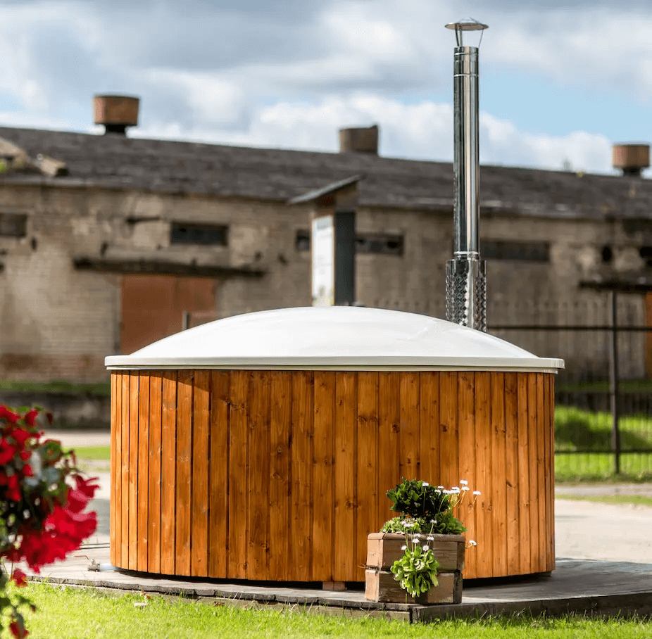 Viking Industrier Fiberglass Hot Tub with integrated heater and closed white lid, placed on a wooden platform with potted flowers in the foreground and an old brick industrial building in the background under a cloudy sky.