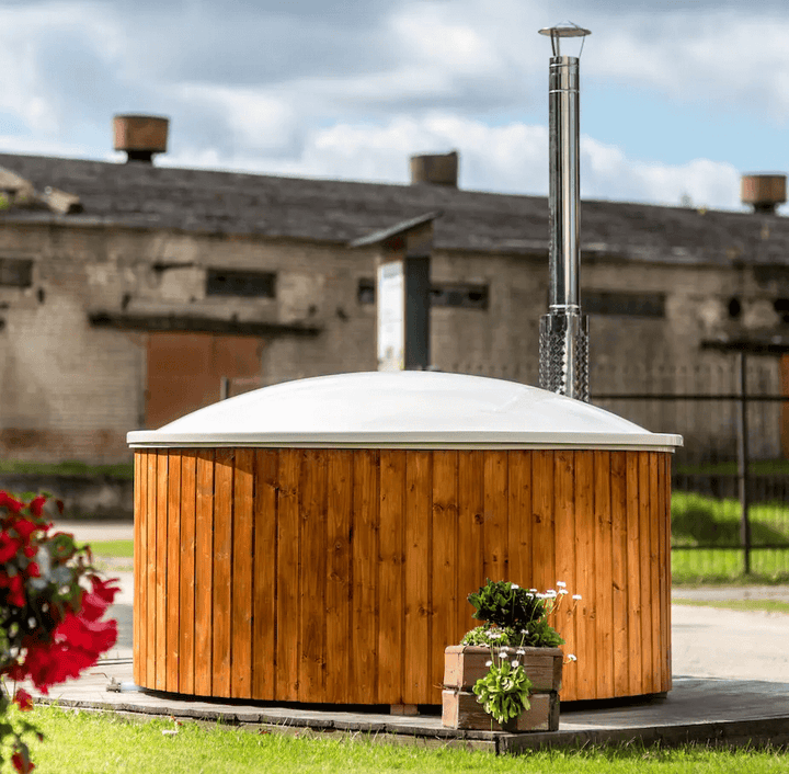 Viking Industrier Fiberglass Hot Tub with integrated heater and closed white lid, placed on a wooden platform with potted flowers in the foreground and an old brick industrial building in the background under a cloudy sky.