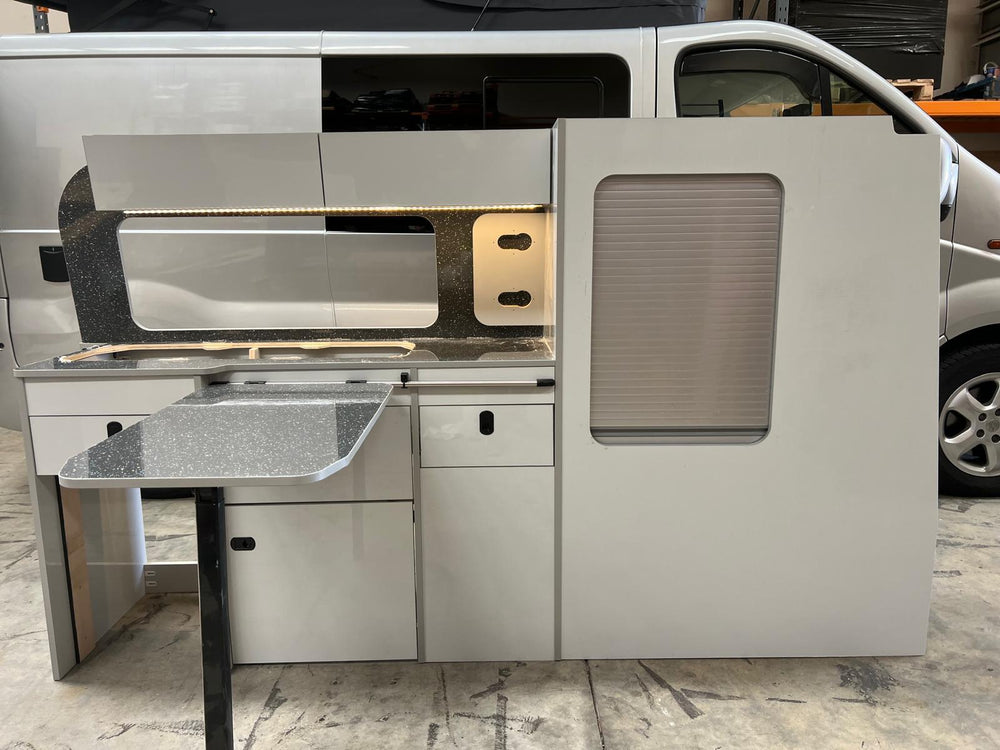 Ford Transit Custom Campervan Kitchen Unit Bespoke installed inside a white van with LED strip lighting, overhead lockers and side tambour door, shown with the van exterior visible in the background.