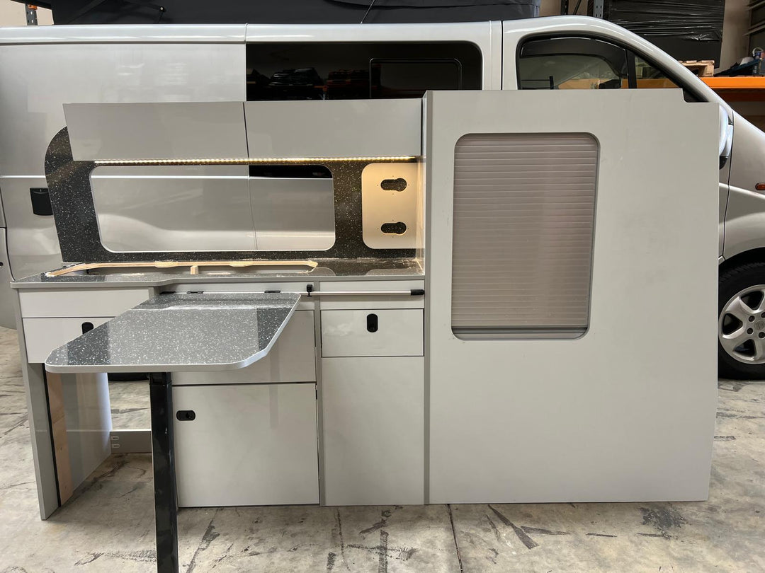 Ford Transit Custom Campervan Kitchen Unit Bespoke installed inside a white van with LED strip lighting, overhead lockers and side tambour door, shown with the van exterior visible in the background.