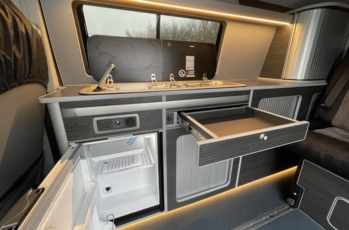 Ford Transit Custom Campervan Kitchen Unit grey wood-effect cabinetry with pull-out drawer and integrated fridge inside camper van interior.