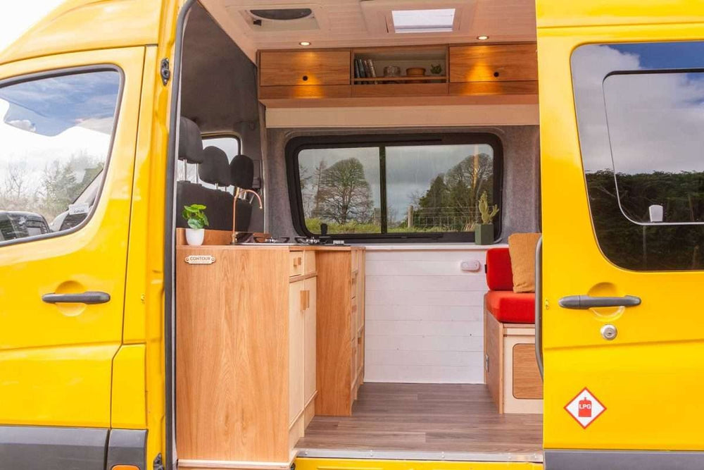 Interior campervan view featuring the Campervan Foss Kitchen Unit installed along the side wall with overhead cabinets and seating area.
