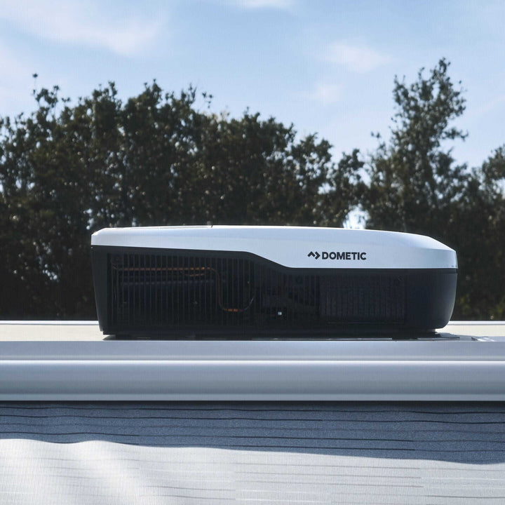 Dometic FreshJet FJX4 1500M Air Conditioner rooftop unit viewed from the side on a motorhome with trees and blue sky in the background.