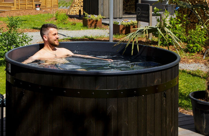Man enjoying a Harvia Legend wood-fired hot tub in a landscaped garden.
