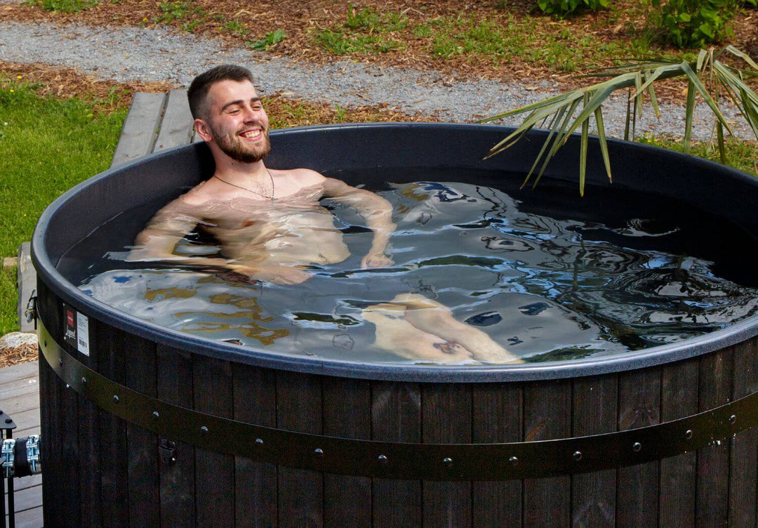 Man relaxing in a Harvia Legend black wooden hot tub outdoors in a modern garden setting.