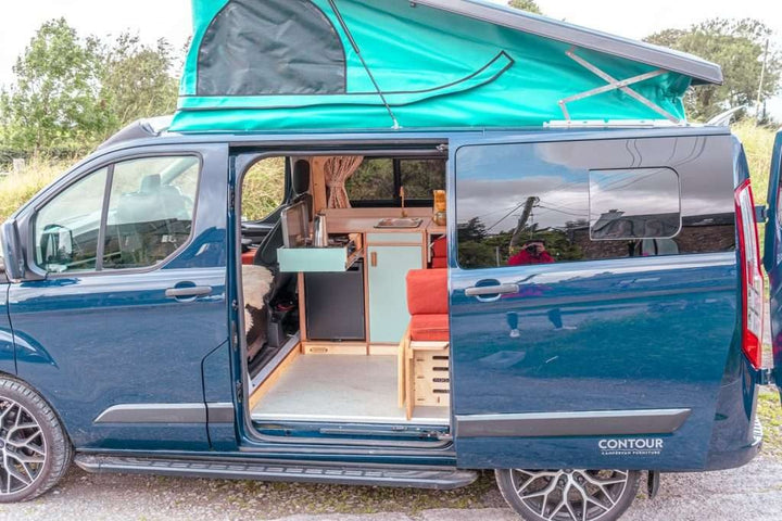 Exterior side view of a campervan with the sliding door open, revealing the Campervan Helm Kitchen Unit and interior seating layout.