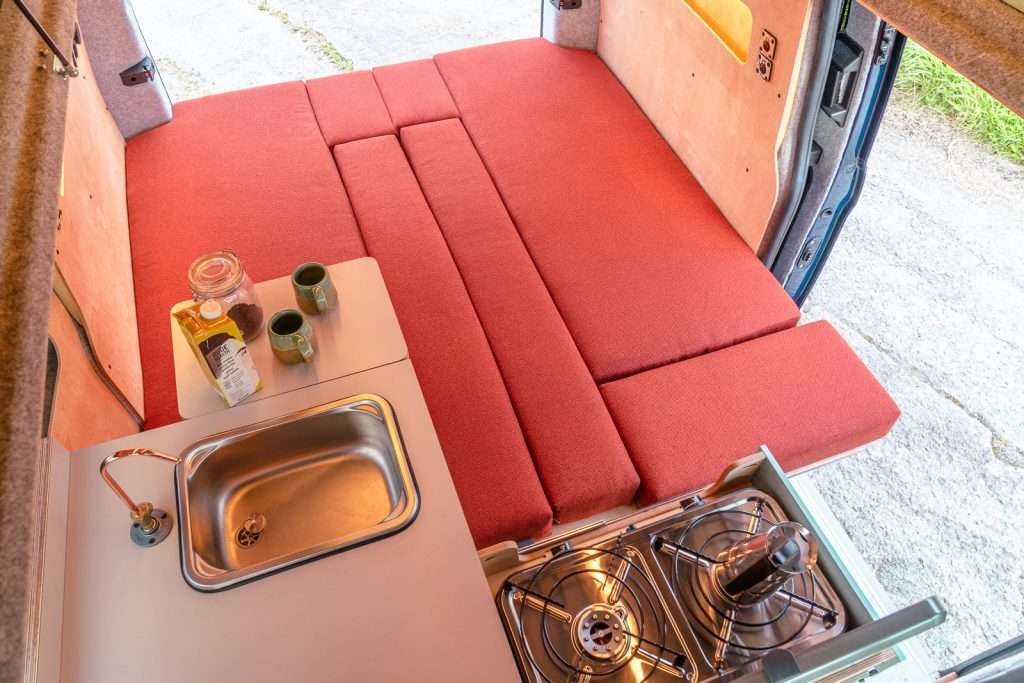 Bed conversion view of the campervan interior showing the seating transformed into a sleeping area next to the Campervan Helm Kitchen Unit.