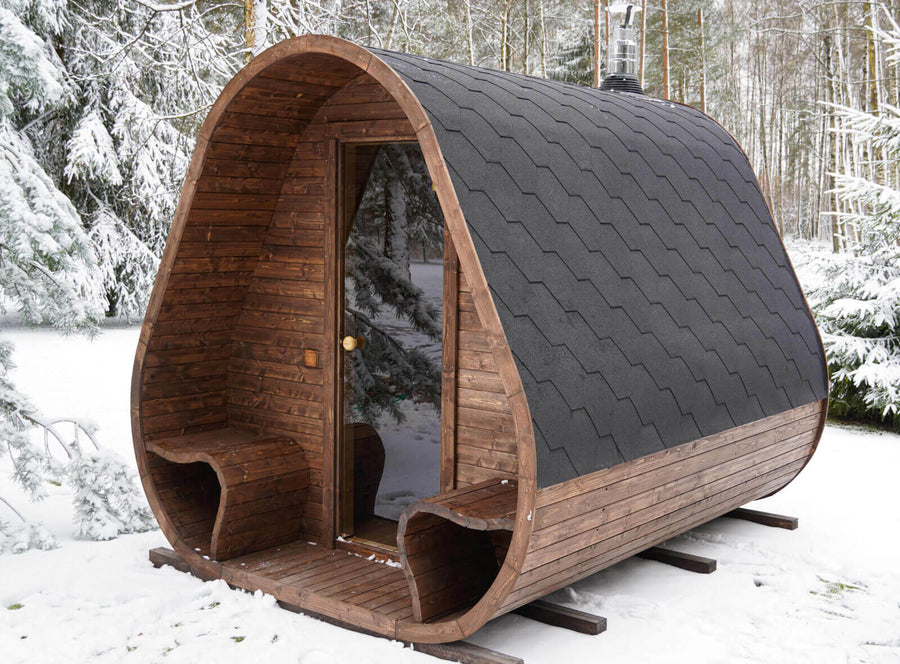Herkus Grand Triangular Outdoor Sauna installed in a snowy woodland setting with glass door and chimney visible.