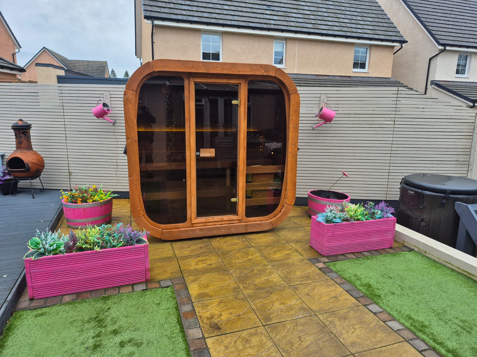 Wooden outdoor Icon 125 sauna pod with pink planters on a patio