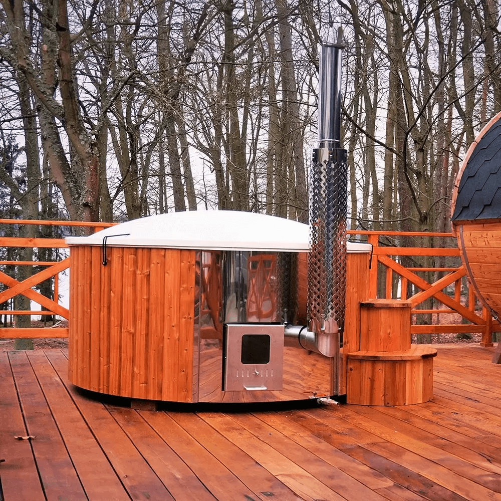 Wood-fired InMedias Delux 200 Hot Tub with white lid and chimney, on a wooden terrace with forest background in winter.