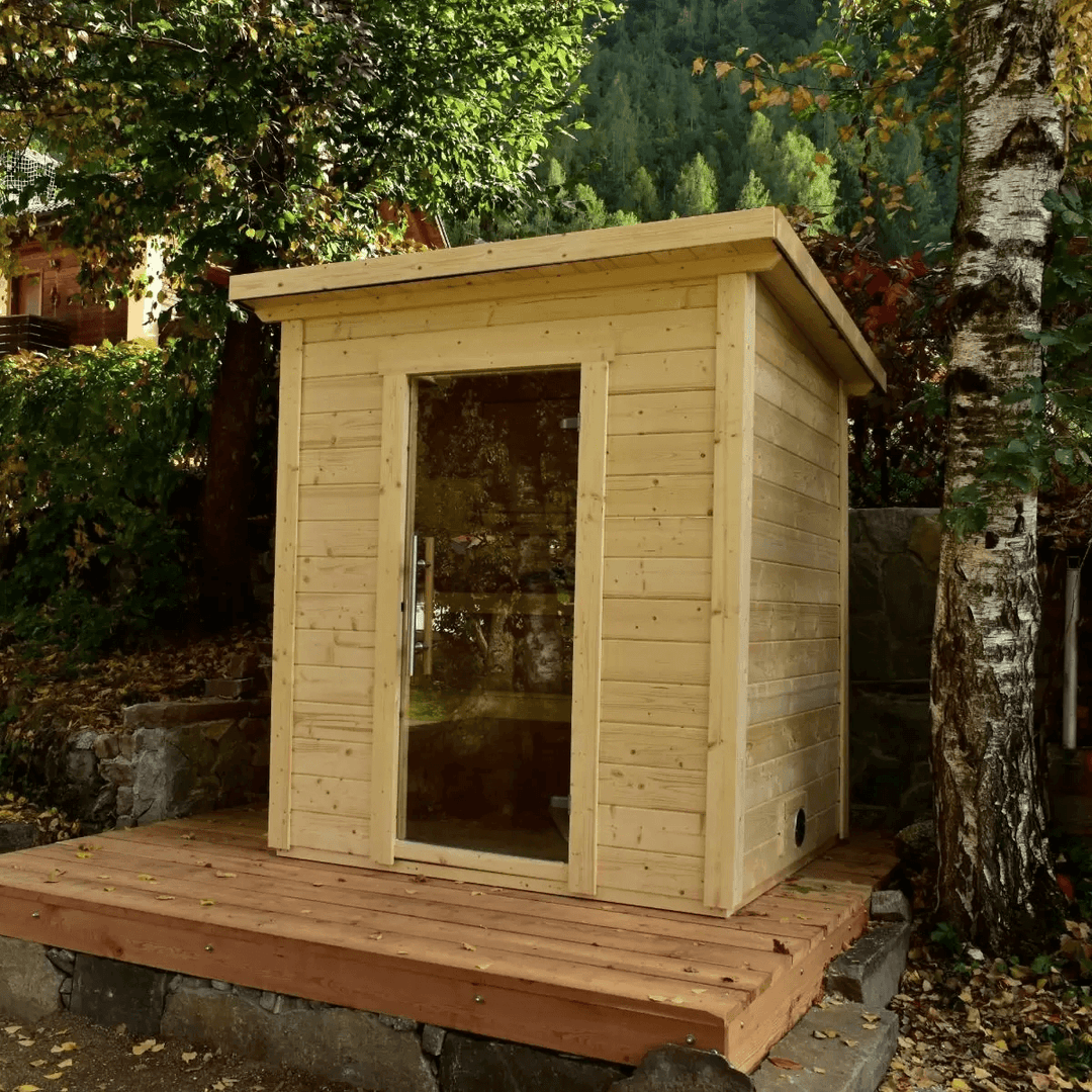 InMedias Brico Log Sauna placed outdoors among trees on a raised wooden platform.
