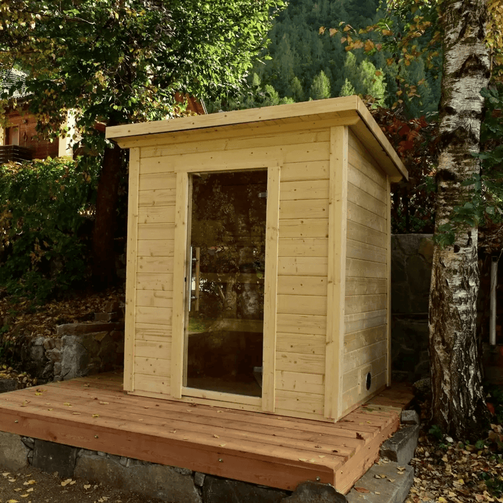 InMedias Brico Log Sauna placed outdoors among trees on a raised wooden platform.