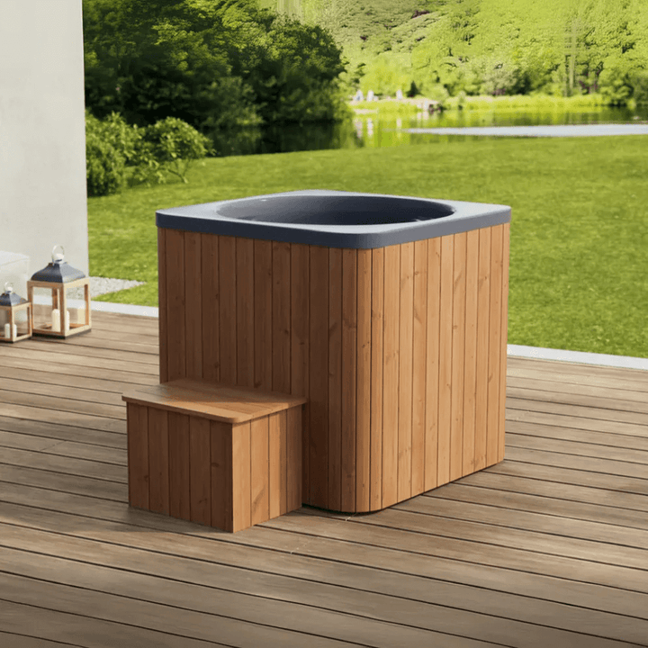 Square wood-panelled cold plunge tub with dark interior and step, placed on an outdoor deck with green landscape in the background.