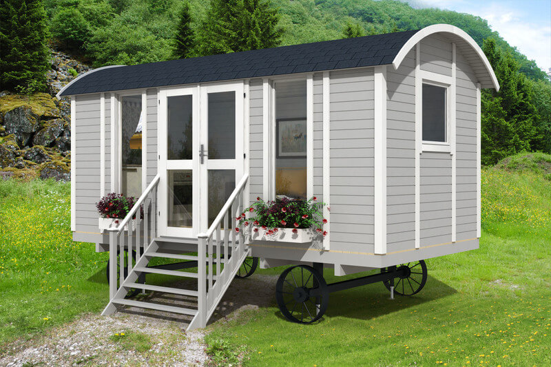 InMedias Modern Shepherd Hut with light grey cladding and white trim, featuring flower boxes and double stairs, surrounded by green hills and trees under a clear sky.