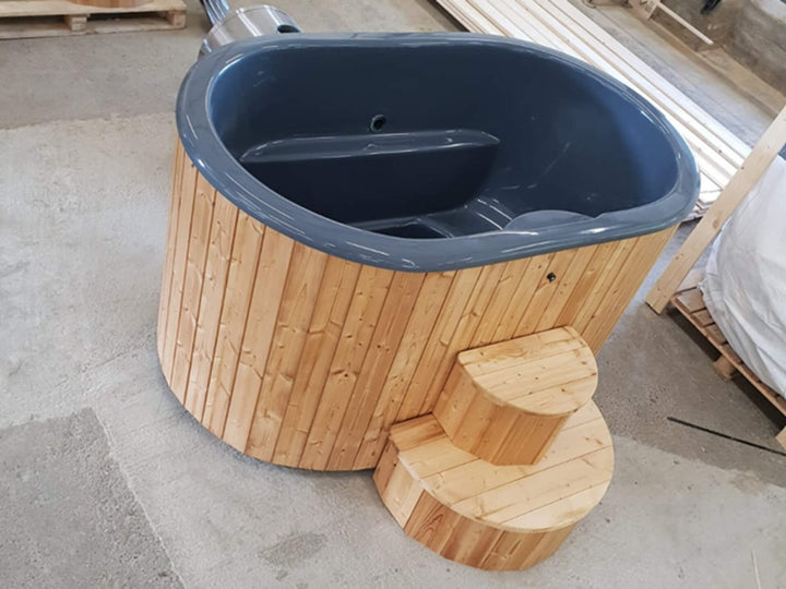 InMedias Ofuro Cold Tub with grey interior and natural wood exterior placed on concrete floor in manufacturing environment.