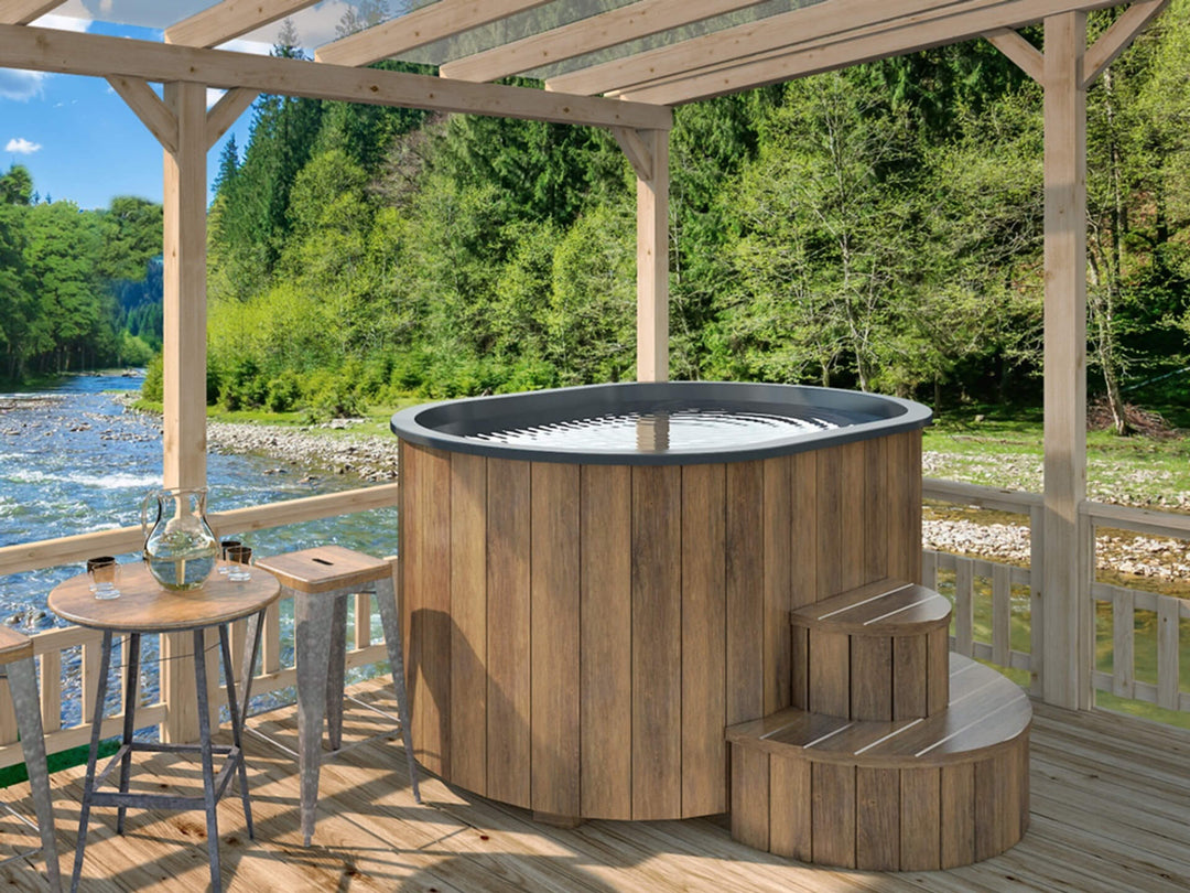 Ofuro Cold Tub with dark wood cladding and black interior on a riverside wooden deck with mountains and trees in the background.