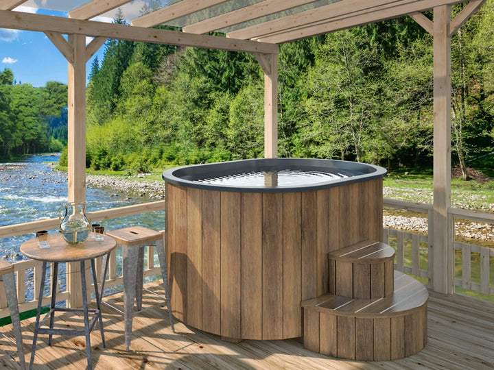 Ofuro Cold Tub with dark wood cladding and black interior on a riverside wooden deck with mountains and trees in the background.