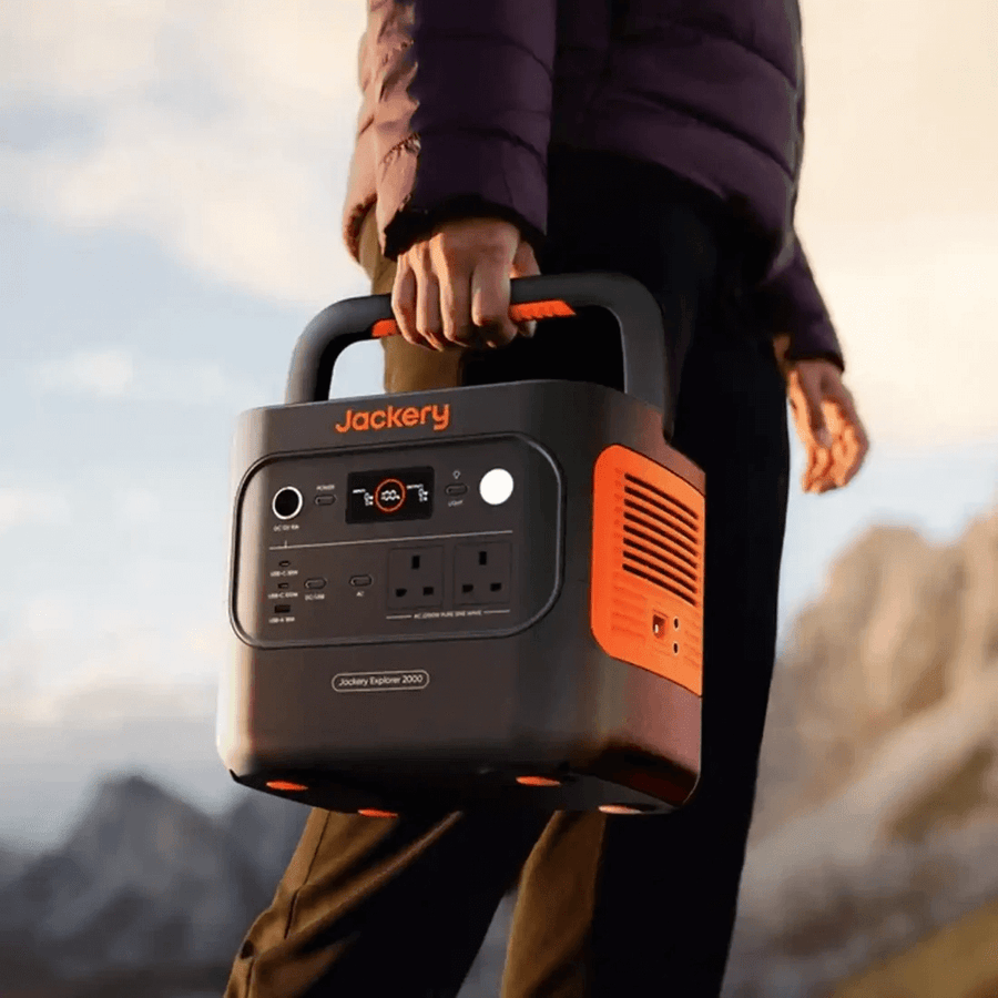 Person holding the Jackery Explorer 2000 V2 portable power station by the handle during sunrise with mountain background.