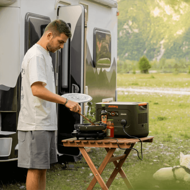 Jackery Explorer 3000 v2 Portable Power Station powering cooking equipment beside a camper van in a grassy outdoor setting.