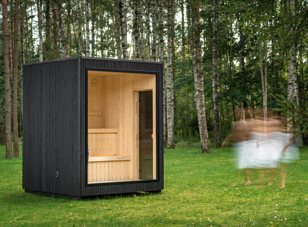 Jonas Classic Outdoor Sauna ebony finish with open glass front, set on grass with blurred person walking nearby.