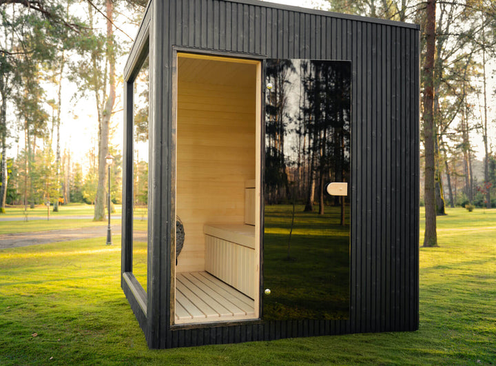 Jonas Classic Outdoor Sauna ebony finish with open glass front, set on grass with blurred person walking nearby