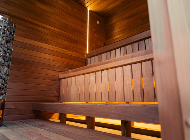 Jonas Grand Classic Outdoor Sauna interior featuring tiered wooden benches with integrated warm LED lighting and sauna heater stones, photographed inside the cabin.