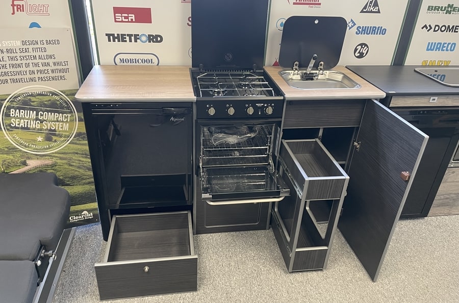 Large Campervan Kitchen Pod with integrated gas oven, four-burner hob, sink, fridge, and pull-out storage drawers in showroom setting.