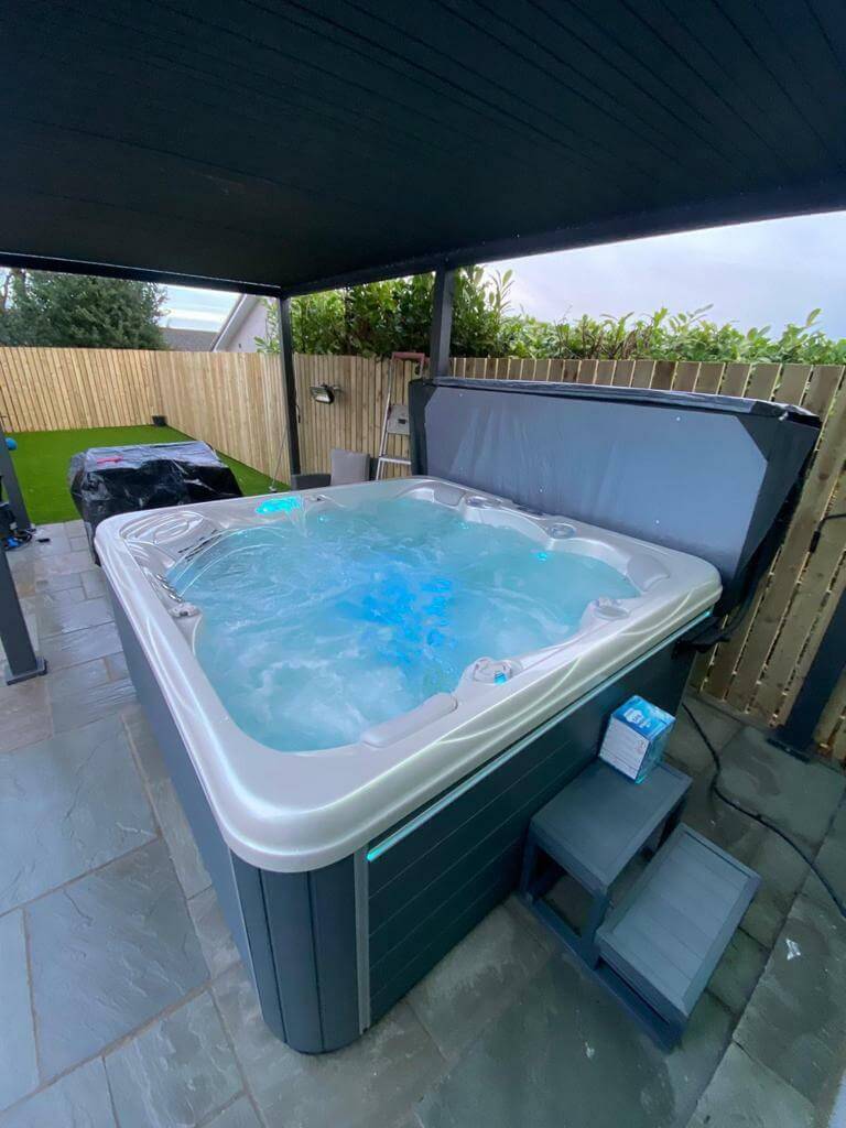 Luso Spas The Luna Hot Tub filled with blue-lit water under a pergola.
