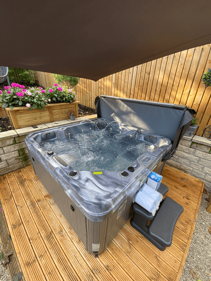 Luso Spas The Hawaii 2 Hot Tub bubbling in use under a large canopy on a wooden deck with flower beds in the background.