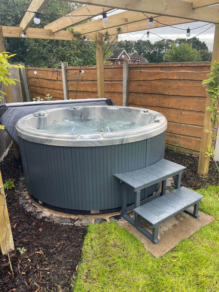 Luso Spas The Zodiac Plug & Play Hot Tub installed under a wooden pergola with string lights in a landscaped garden.