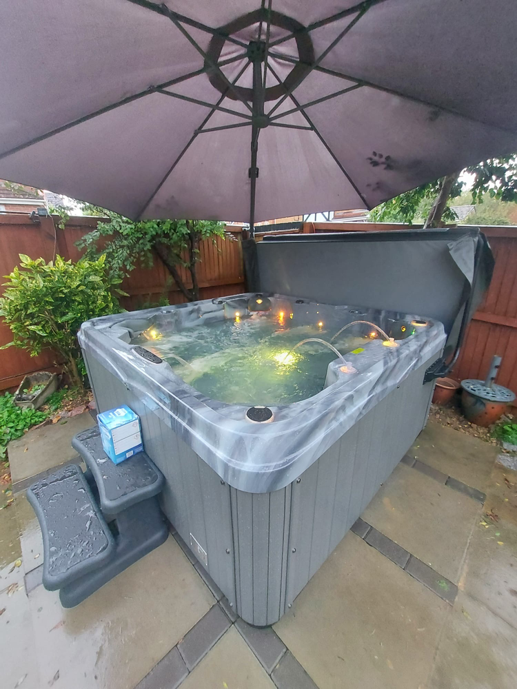 Luso Spas The Venice 2 Hot Tub under an umbrella with green LED lighting in a backyard setting.