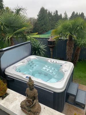 Luso Spas The Vepo Hot Tub placed in a backyard garden with steps and tropical plants surrounding it.