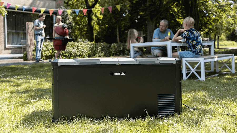Mestic MCCP-90 cool box compressor outdoors on grass during a family gathering.
