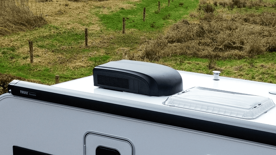 Mestic RTA-1700L Rooftop Air Conditioner in black installed on a caravan roof with a grassy field in the background.