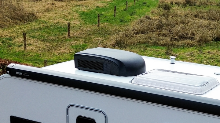 Black Mestic RTA-2500L rooftop air conditioner installed on a caravan roof in an outdoor setting.